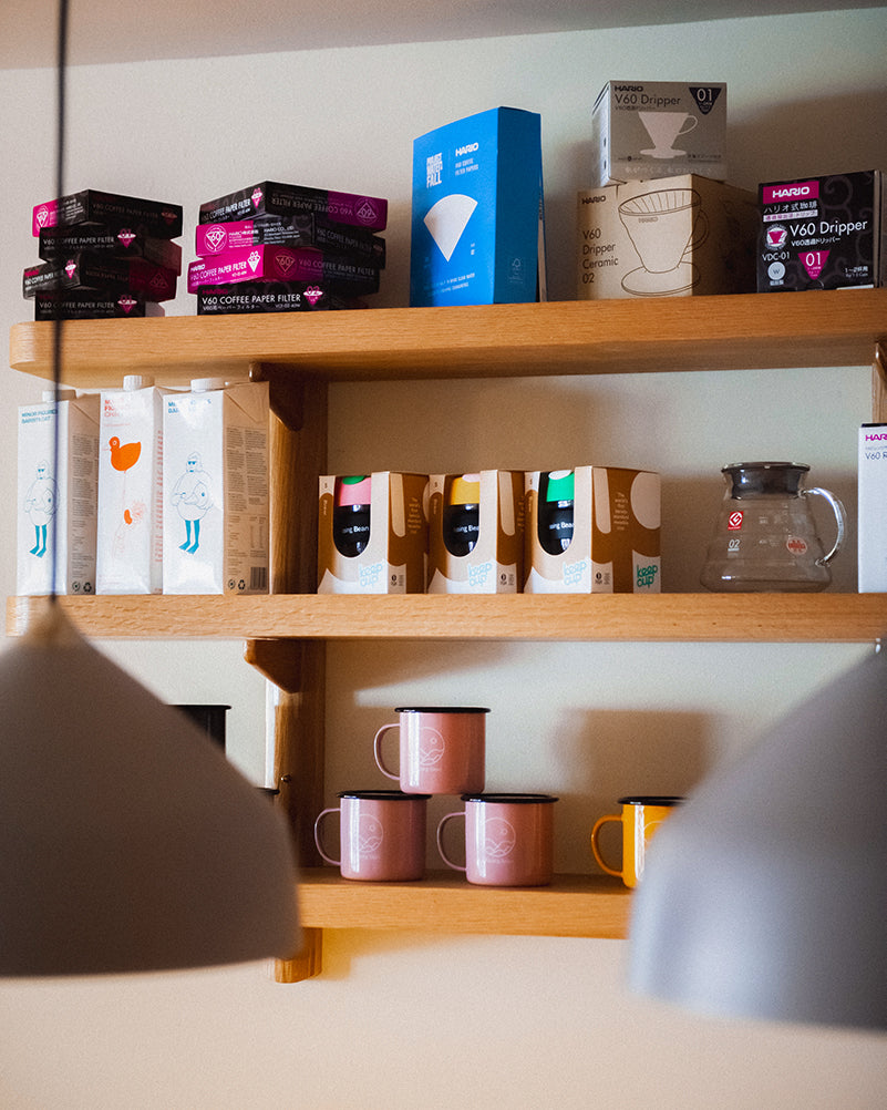 Wooden shelves displaying Missing Bean mugs, Minor Figures milk, keep cups, Hario brewing equipment, V60s and paper filters at Missing Bean's cafe in Botley