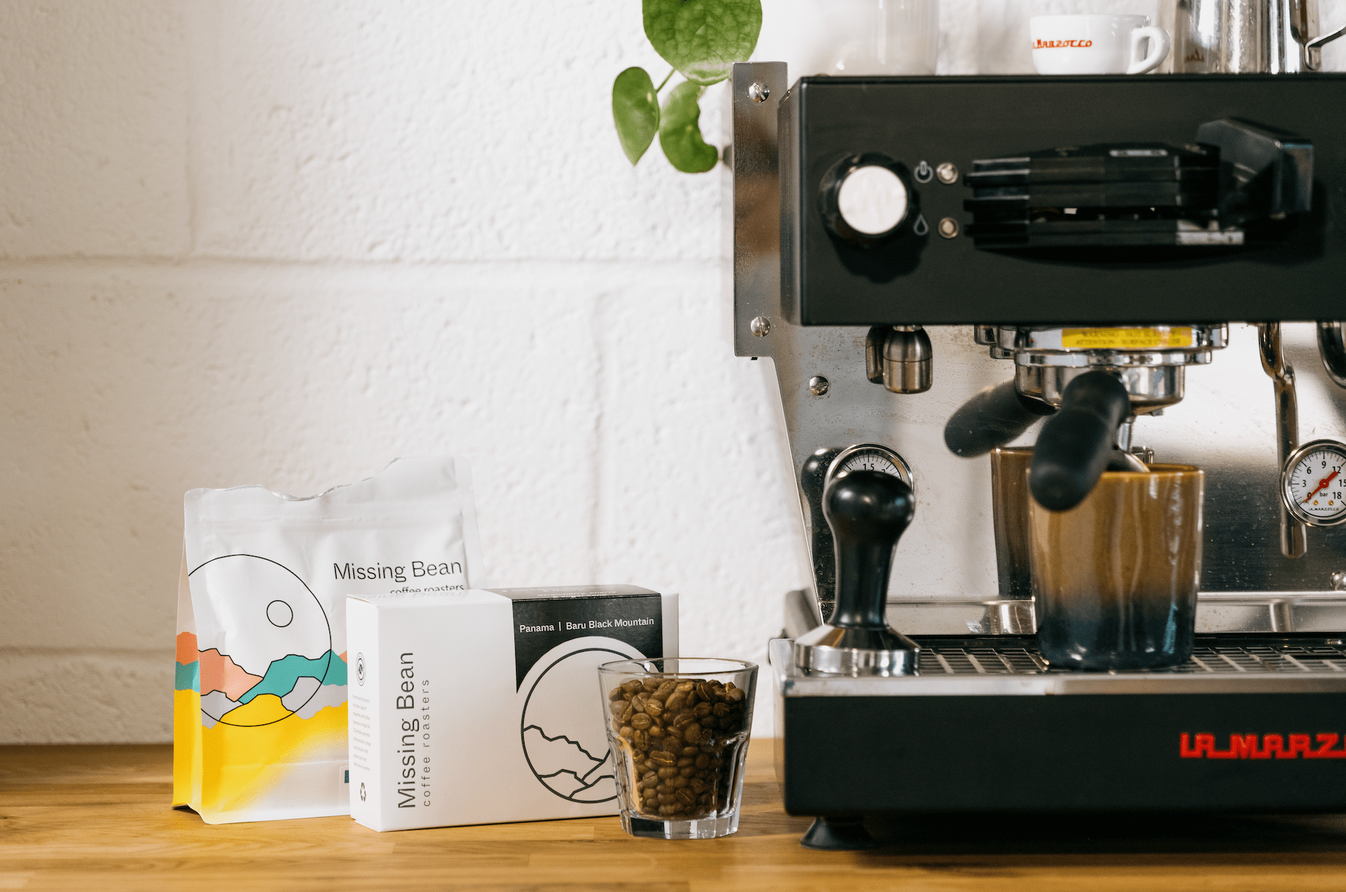 Coffee machine and coffee beans at Missing Bean, with packaged coffee and a glass of coffee beans on a wooden counter.