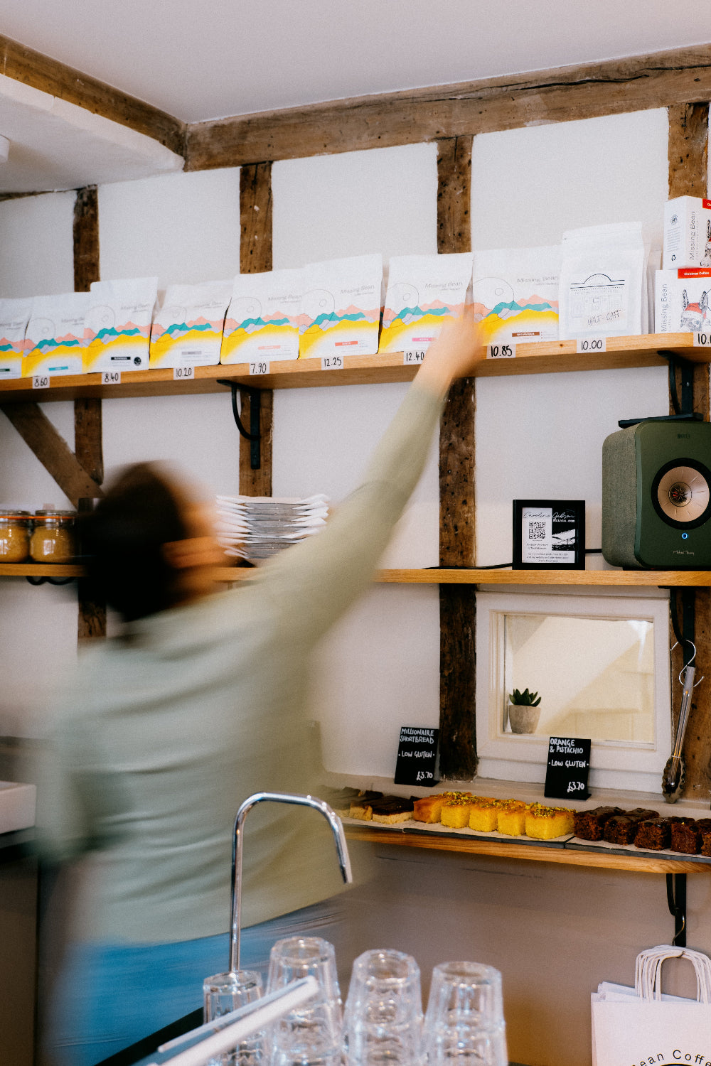 A barista reaching up towards a shelf of 250g Missing Bean coffee bags behing the counter of Missing Bean's Woodstock cafe.