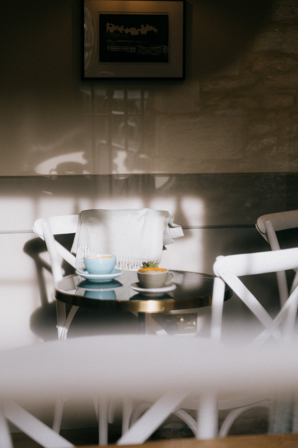 Shot through the window of Missing Bean's Woodstock cafe, two cappuccinos on top of a black table. There is a white scarf daped over the back of a white chair. 