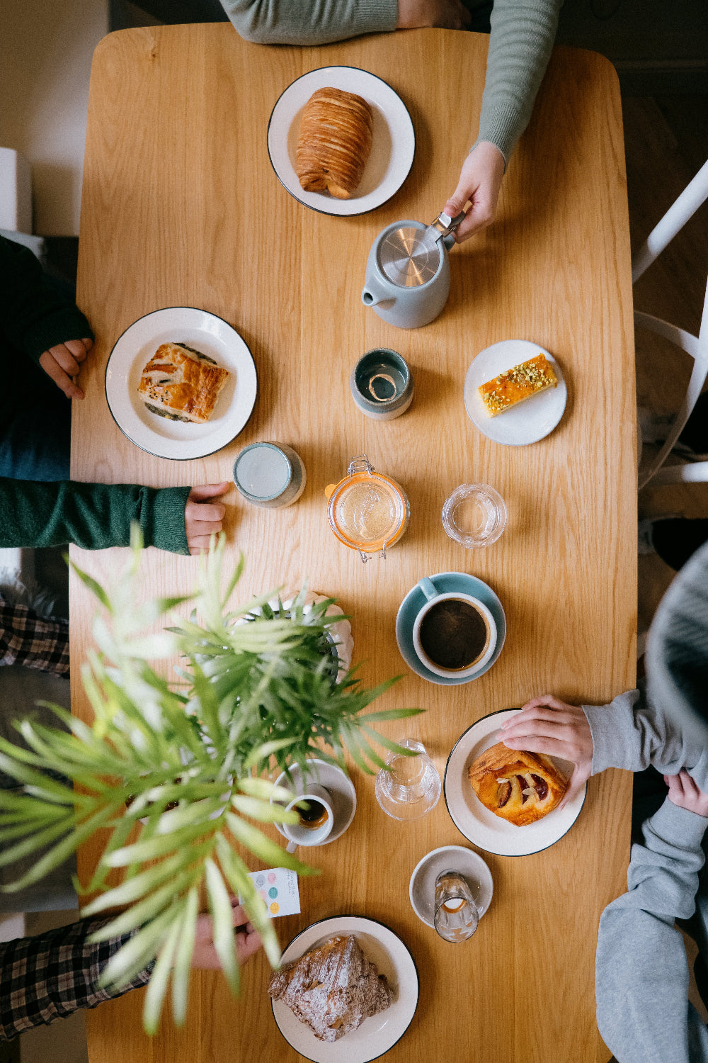 Overhead shot of four people sitting around a wooden table at Missing Bean's Woodstock café. There are various pasties and drinks on the table, and a green plant.