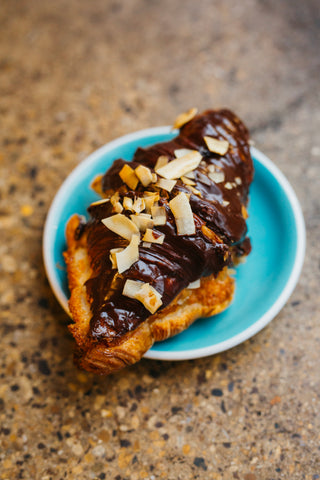 Missing Bean's Bounty croissant with chocolate and coconut on a small blue plate against a brown mottled background