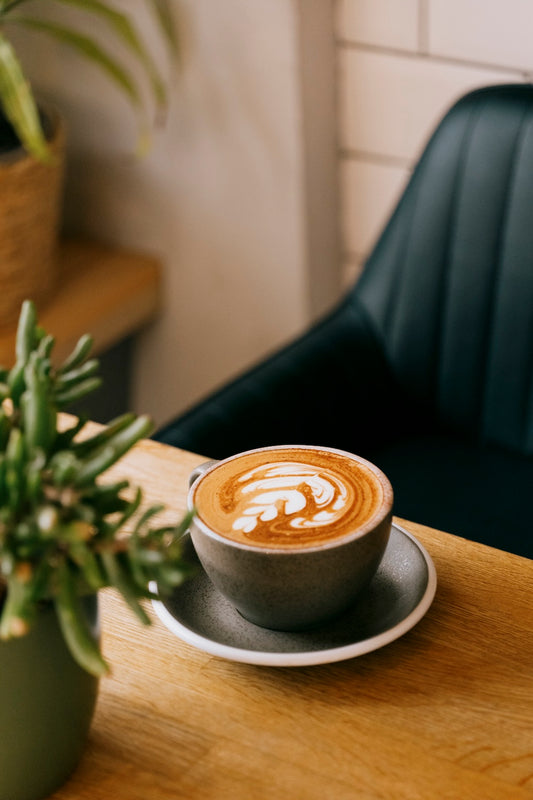 Cappuccino with latte art on a wooden table with a plant and chair in the background