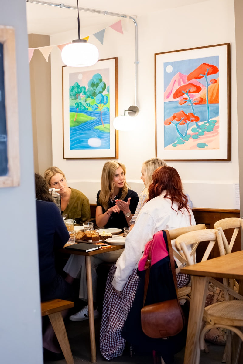 Missing Bean's Charlbury cafe with four people seated at a wooden table, surrounded by colourful framed art on the wall and hanging pendant lights.