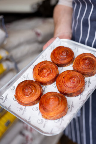 Bakery holding a tray of freshly baked blood orange swirls in Missing Bean's bakery