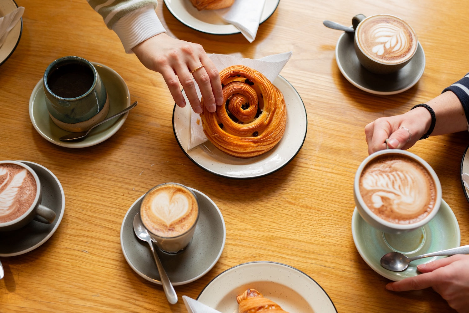 People enjoying a table of coffee and pastries in a cafe setting.