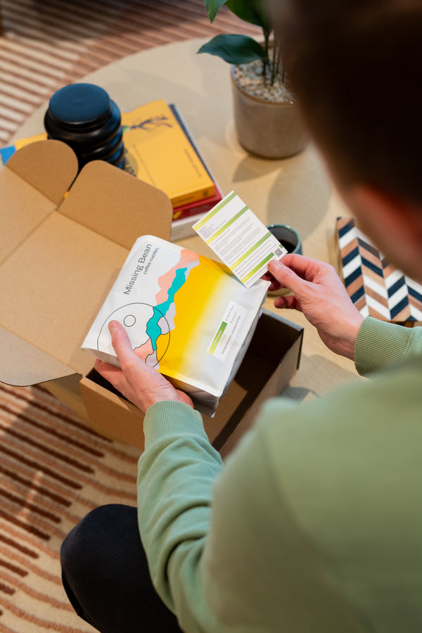 Person opening a subscription box containing Missing Bean Coffee Beans in a home setting.