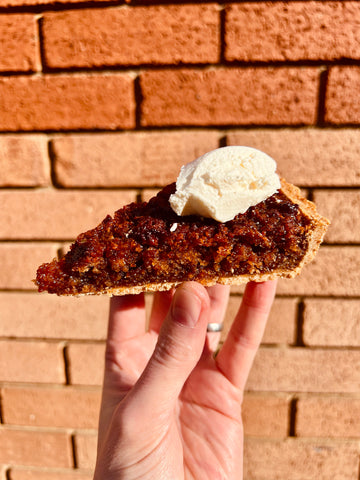 Slice of pecan pie with ice cream held in front of a brick wall