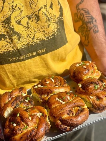 Person wearing a yellow t-shirt with a graphic design, holding a tray of wild garlic scones.