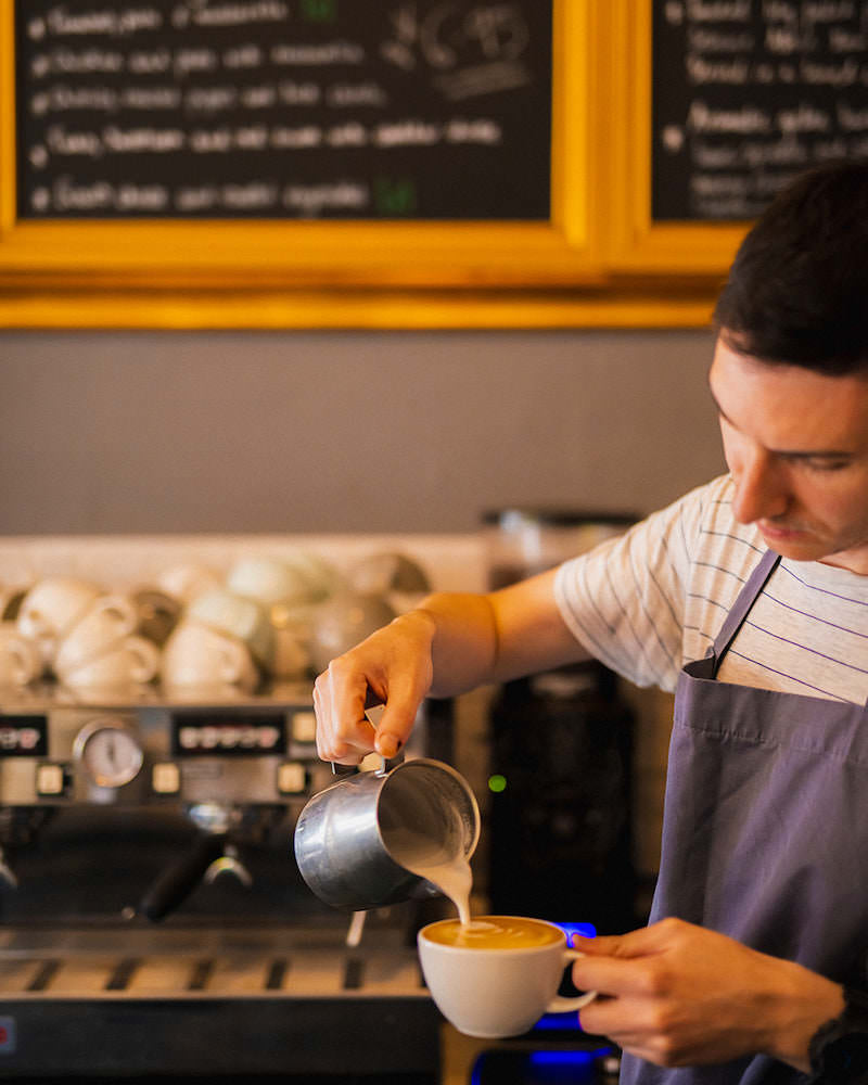 Branca Barista creating latte art with Missing Bean Coffee in front of a coffee machine