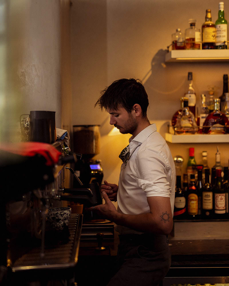 Thyme barista, wearing a white shirt with sleeves rolled up, operating a coffee machine, using Missing Bean wholesale coffee beans
