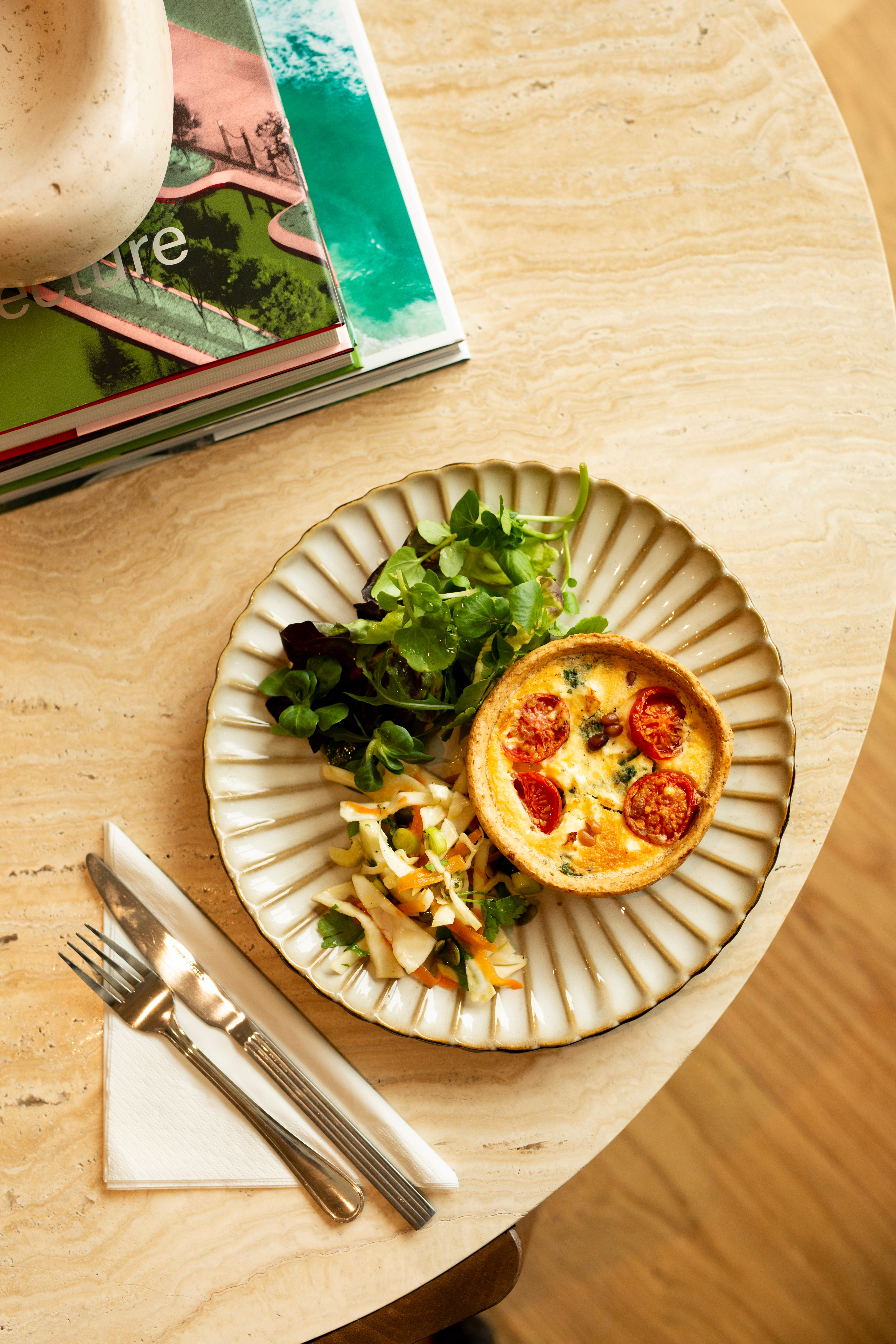 Small plate with a quiche and salad on a wooden table with a magazine in the background.