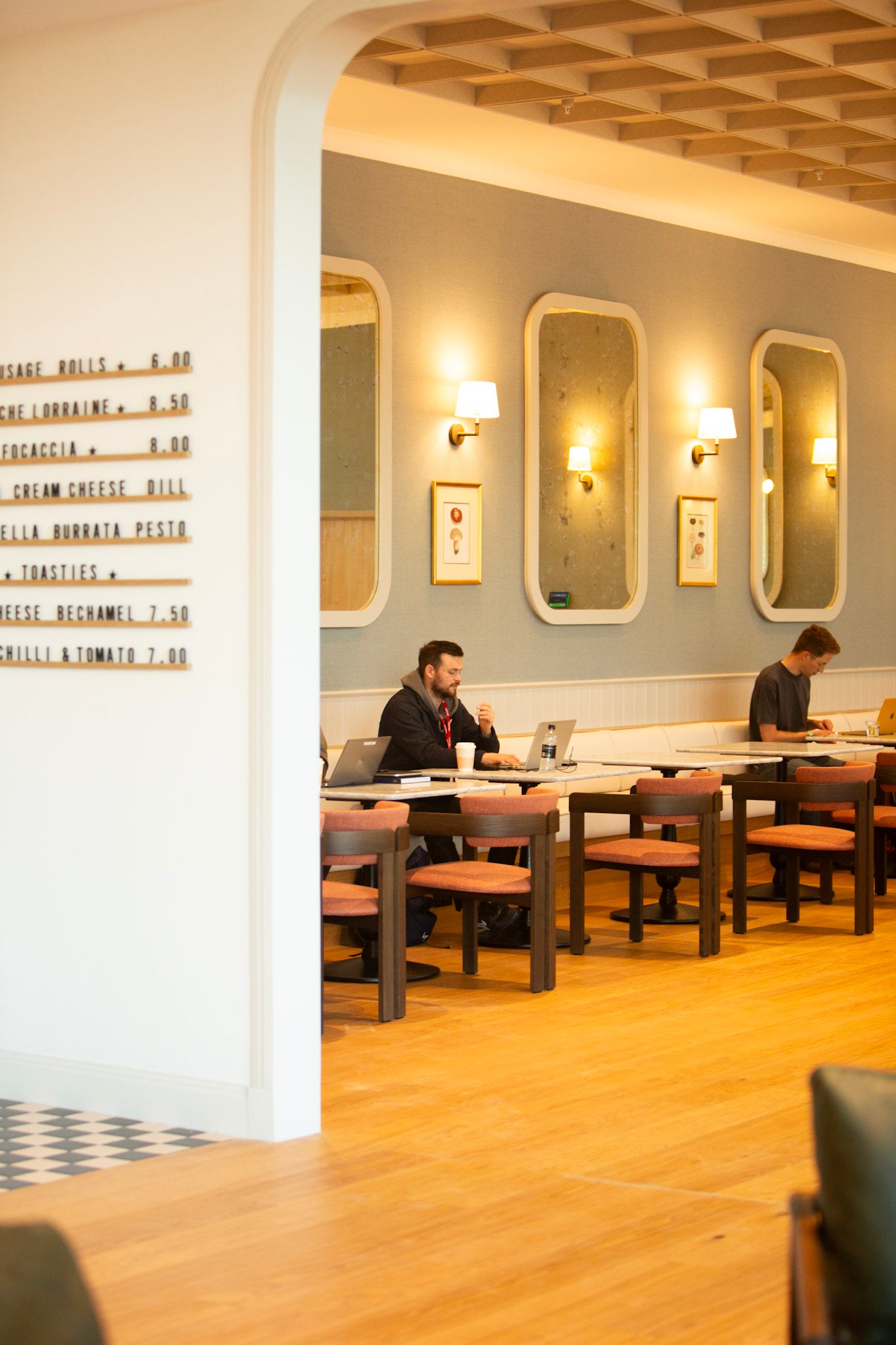 Interior of Missing Bean's Cowley café with tables and chairs, people sitting, on laptops and a wall with art and mirrors.