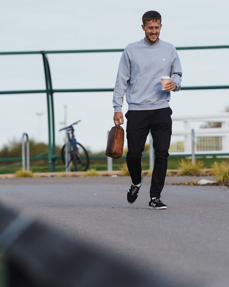 Oxford United midfielder Will Vaulks walking outdoors holding a Missing Bean coffee cup and a bag.
