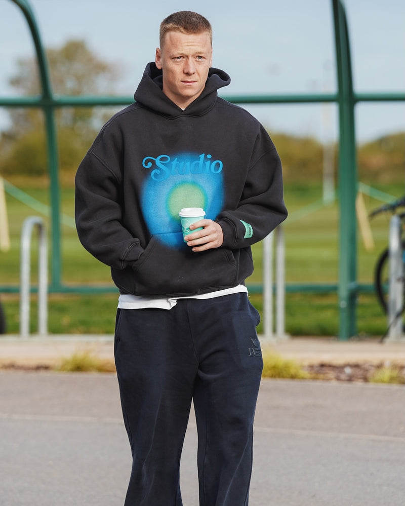Oxford United Midfielder, Brian De Keersmaecker wearing a black hoodie with 'Studio' design, holding a Missing Bean coffee cup outdoors.