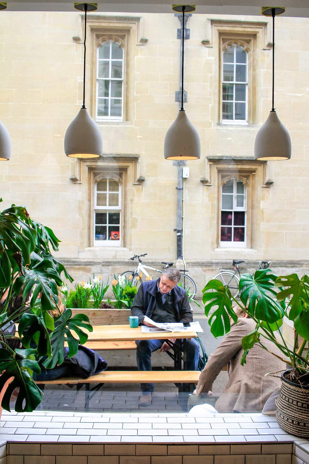 Man reading a newspaper on outdoor seating at Missing Bean Turl street coffee shop in Central Oxford