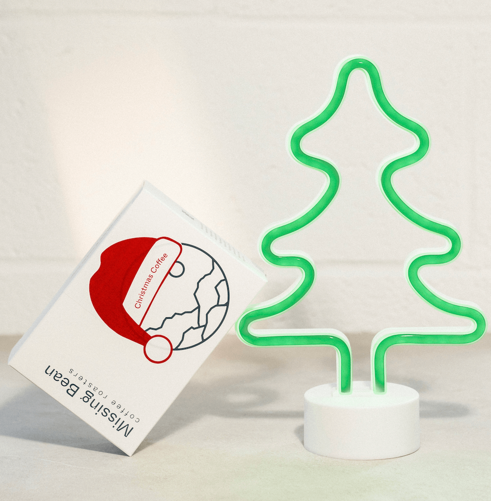 Missing Bean's Christmas Coffee leaning against an led green Christmas tree