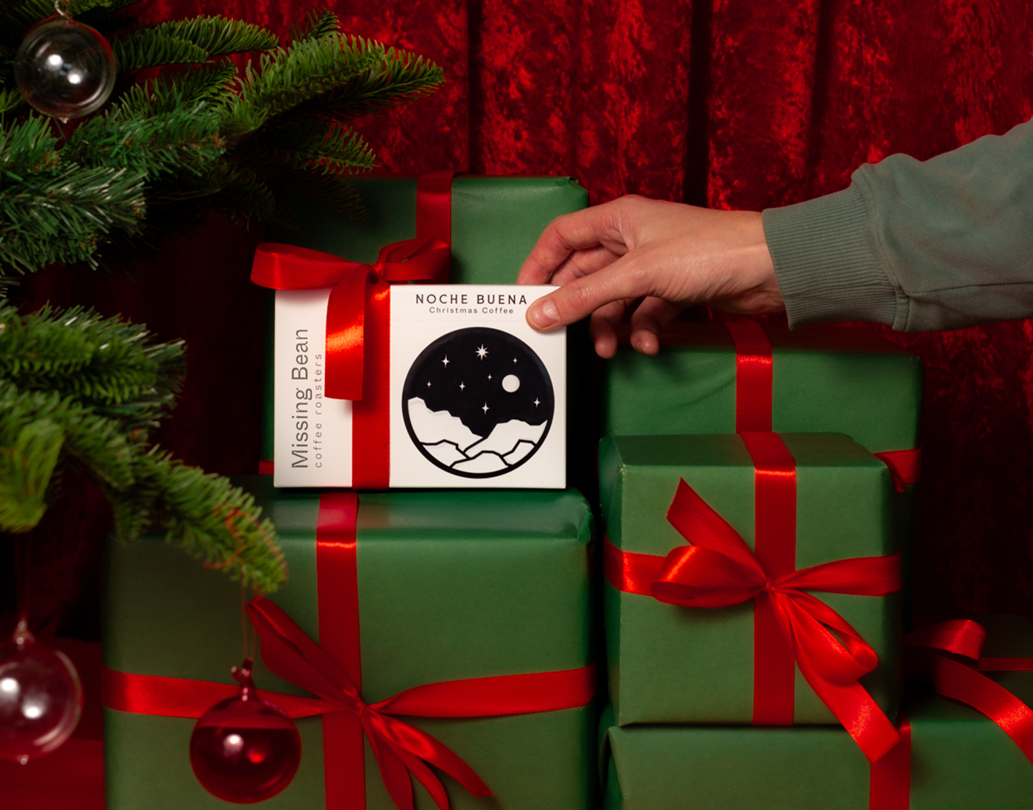 Person placing Missing Bean's Christmas coffee amongst wrapped presents under a Christmas tree.