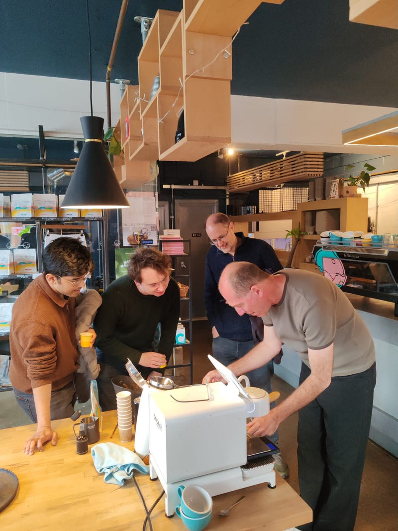 Four people gathered around a Decent Espresso machine on a table at Missing Bean's Roastery, during a hands-on home espresso masterclass.