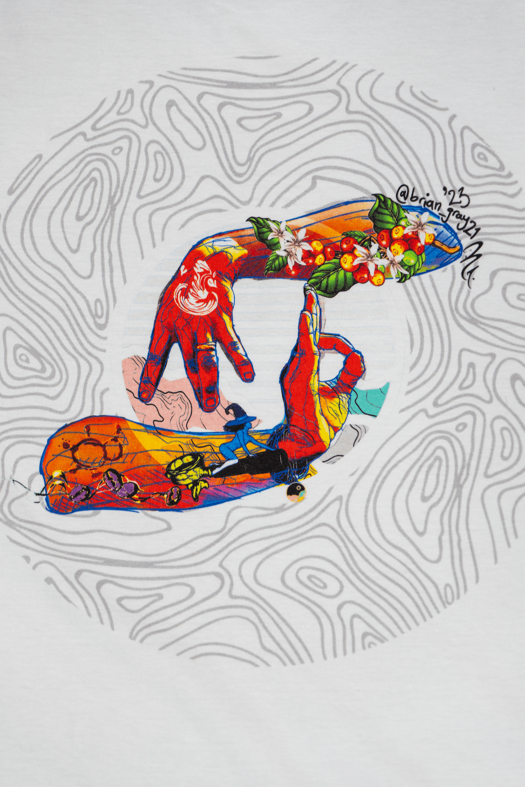 Close up detail of a white Missing bean X Brian Gray T-Shirt featuring a colorful graphic design on the back, depicting two hands spelling out MB which are detailed with a range of clever, original, sketches to signify the journey of a coffee bean.
