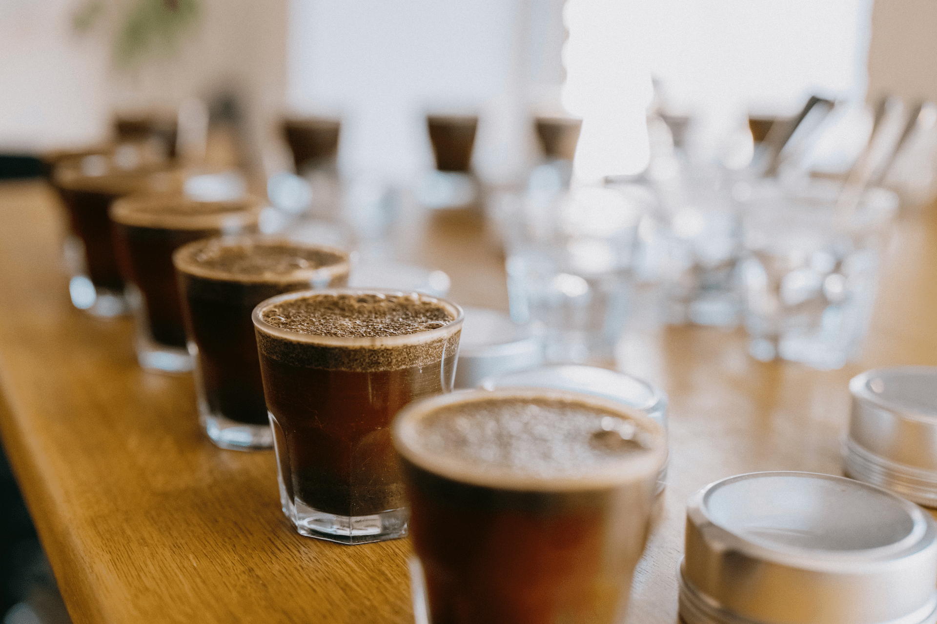Various glasses of coffee on a wooden table arranged for a cupping session, a process for tasting and evaluating coffee roasts.