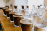 Various glasses of coffee on a wooden table arranged for a cupping session, a process for tasting and evaluating coffee roasts.