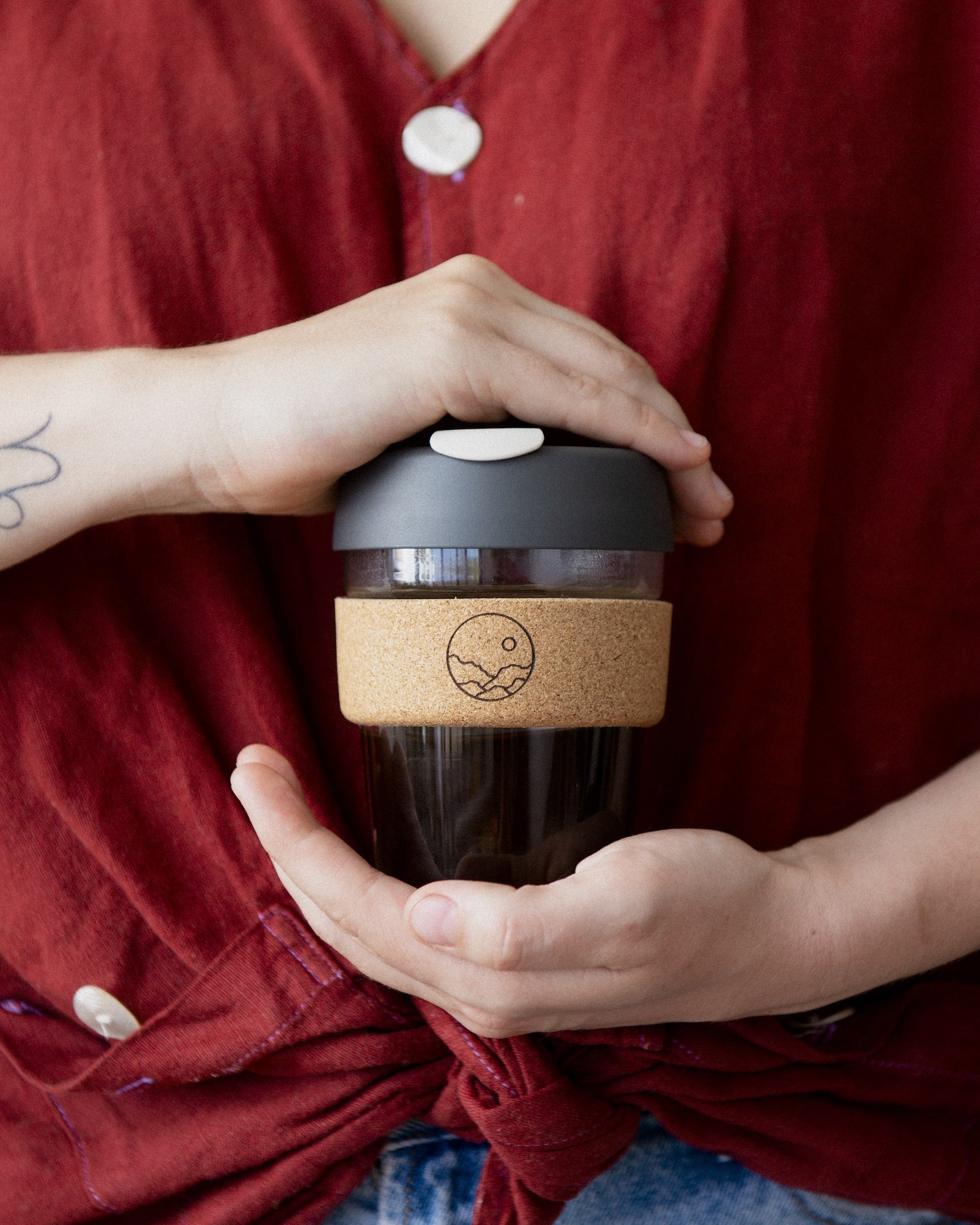 An individual holding a Keep Cup, a glass takeaway coffee cup with a cork heat-proof band.
